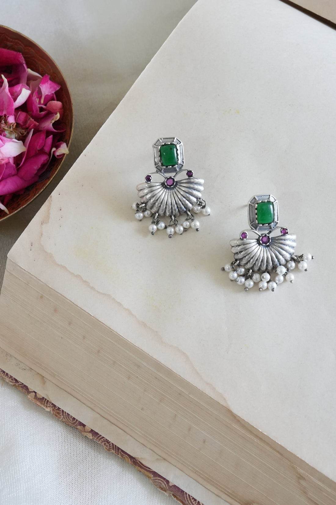 Silver earrings with green and purple stones on a white surface