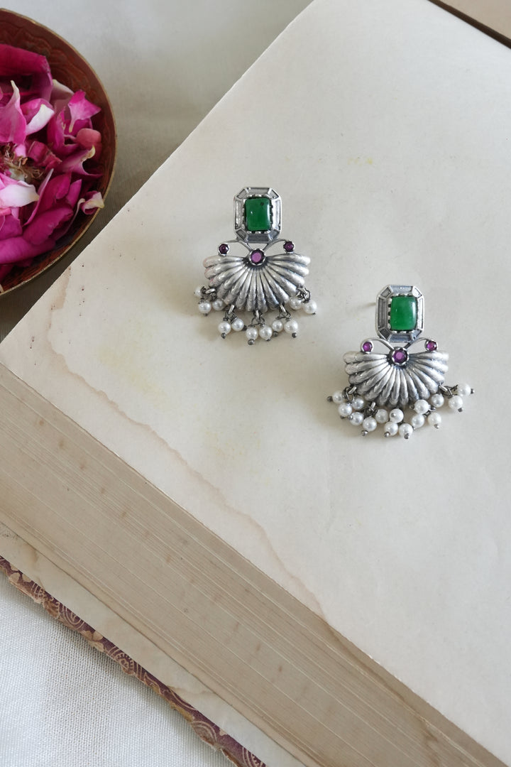 Silver earrings with green gemstones on a light wooden surface.