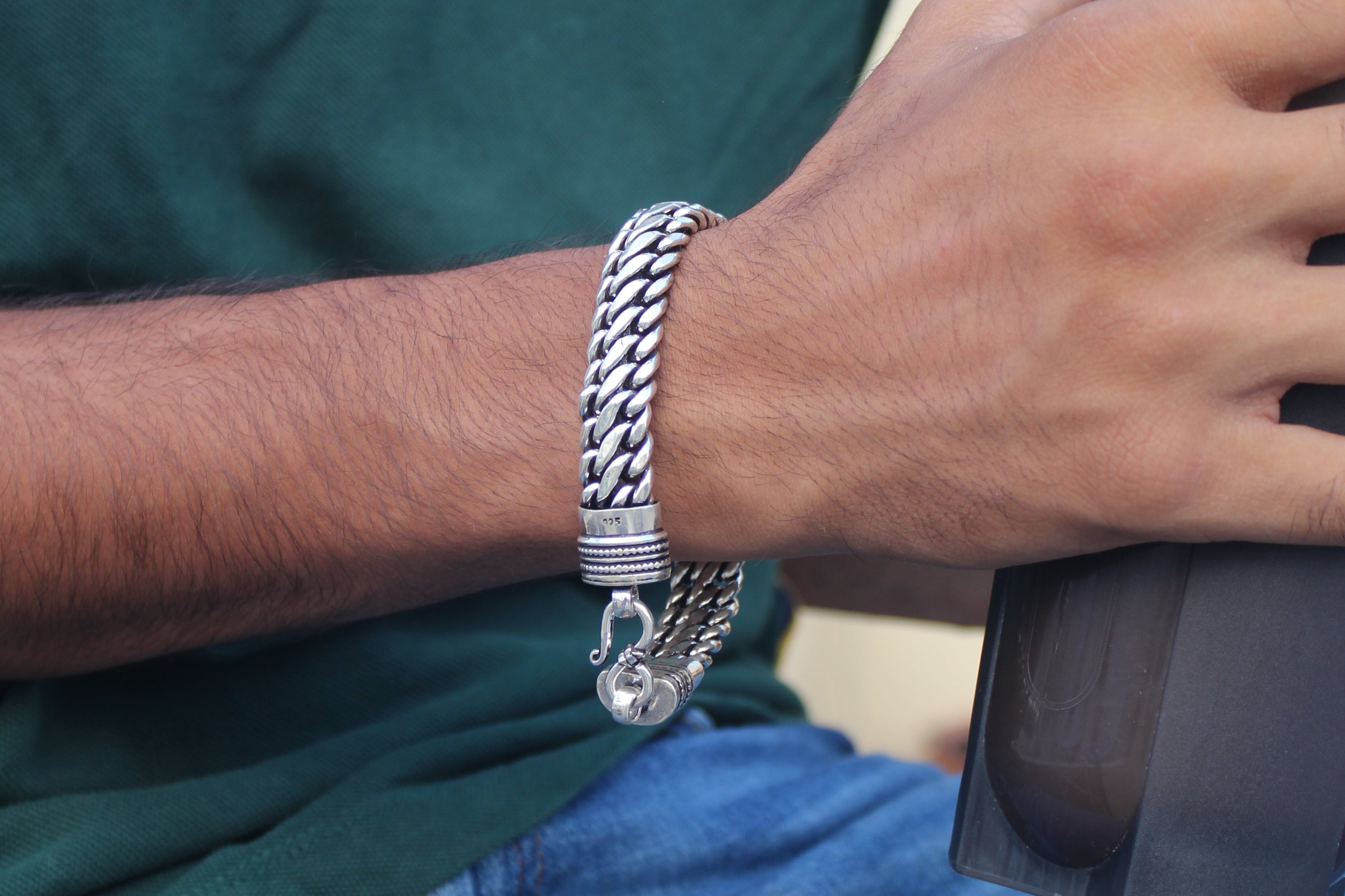 Person wearing a silver bracelet holding a black object, with a focus on the hand and bracelet.
