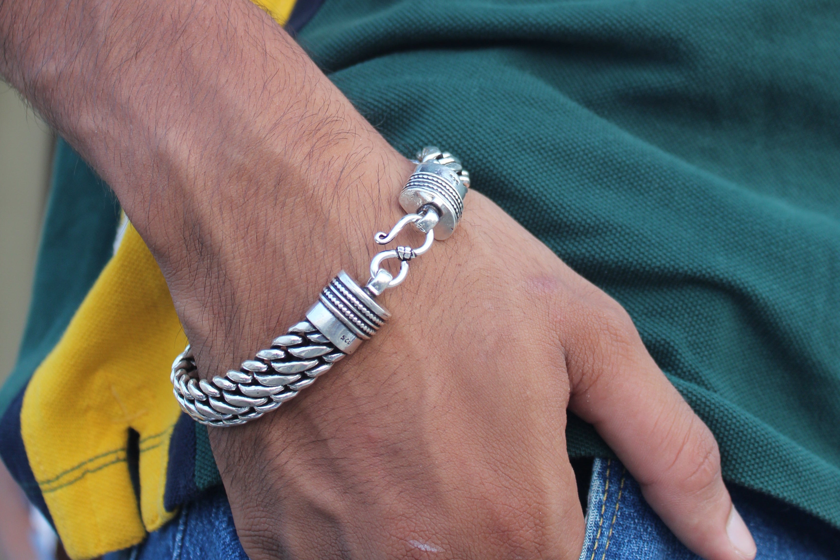Hand wearing a silver bracelet on a green and yellow garment