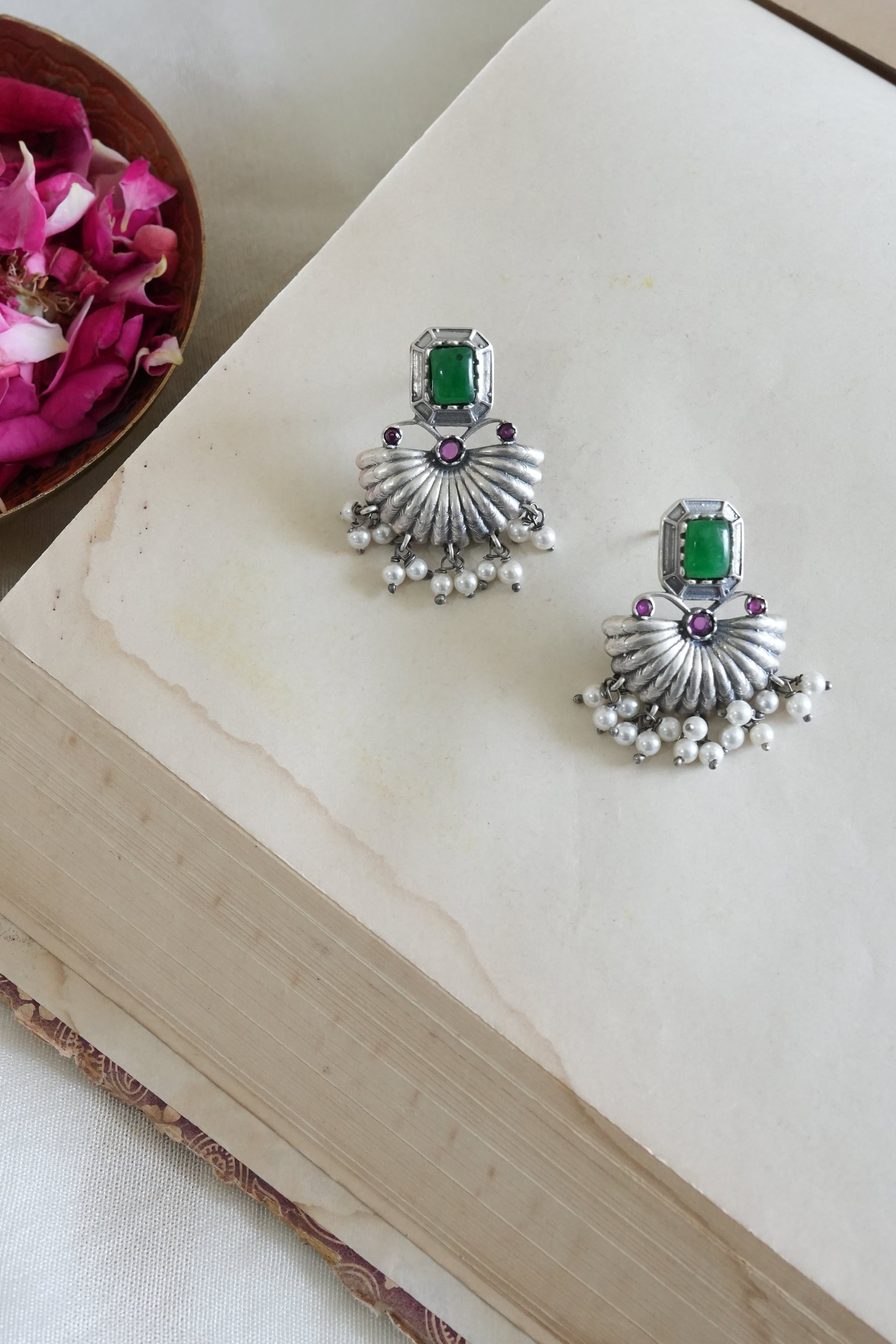 Silver earrings with green gemstones on a light wooden surface.