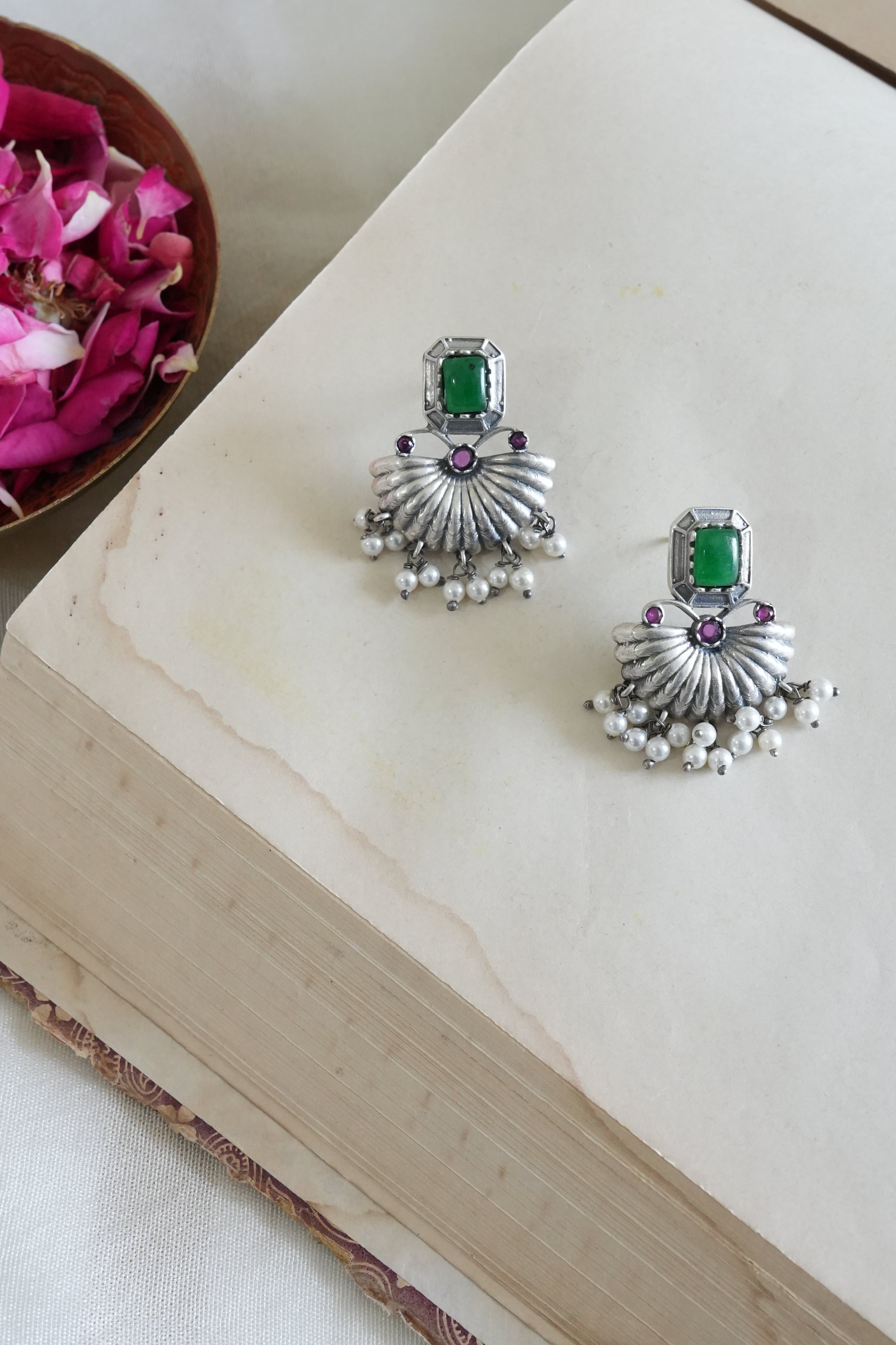 Silver earrings with green gemstones on a wooden surface with pink flowers in the background